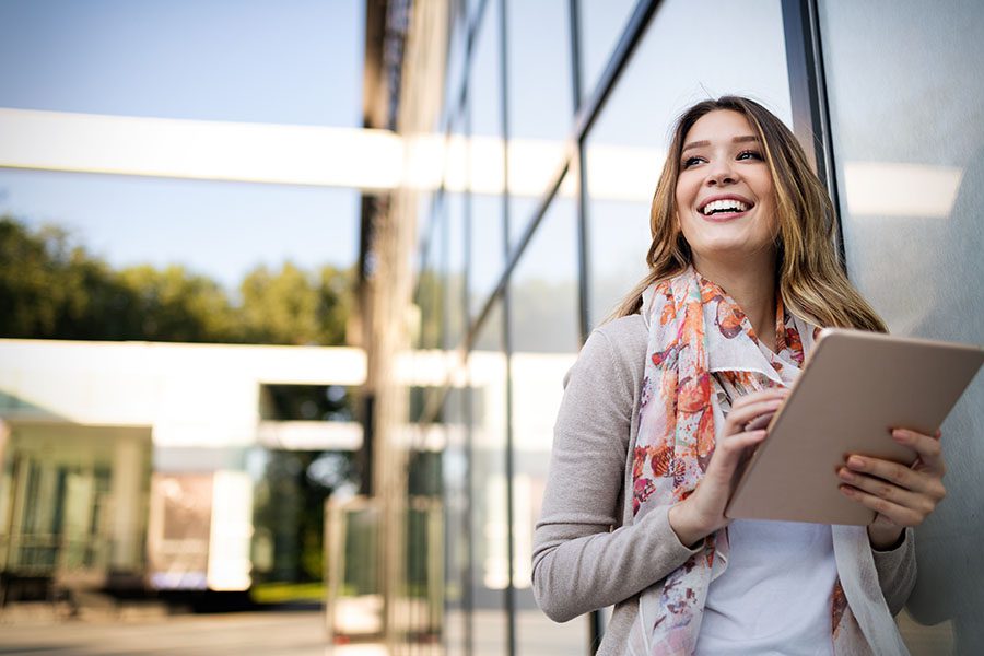 Client Center - Closeup View of Smiling Business Woman Standing Next to a Modern Office Building Using a Tablet