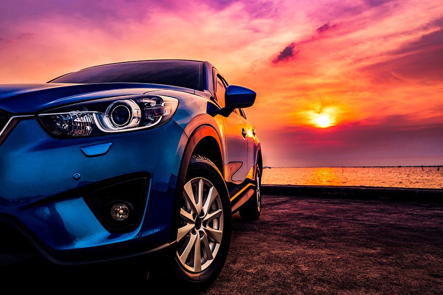 Auto Insurance - View of a Blue Compact SUV Car Parked on a Concrete Road by the Ocean at Sunset