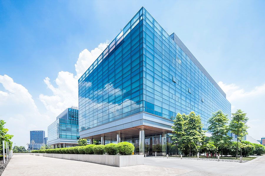 Commercial Property Insurance - View of Modern Glass Commercial Office Building Exterior with Green Landscaping Against a Bright Blue Sky