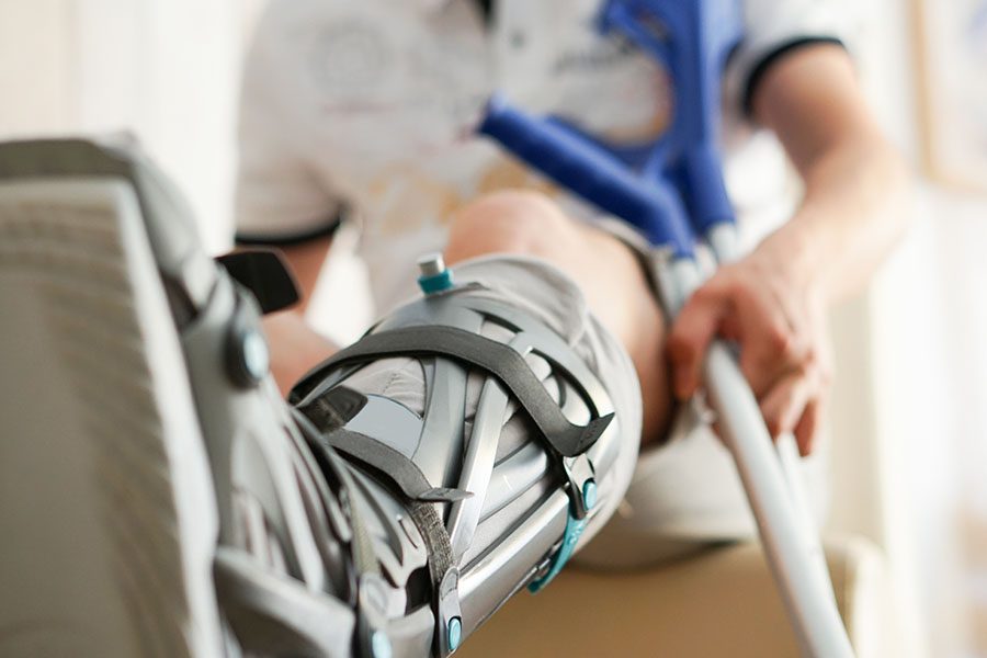Disability Insurance - Closeup View of a Patient Sitting in a Hospital Bed with a Cast Around His Foot as He Holds Crutches