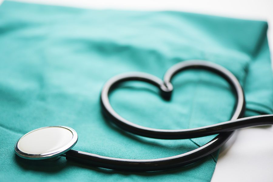 Group Health Insurance - Closeup View of a Stethoscope in a Heart Shape Laying on Green Medical Scrubs